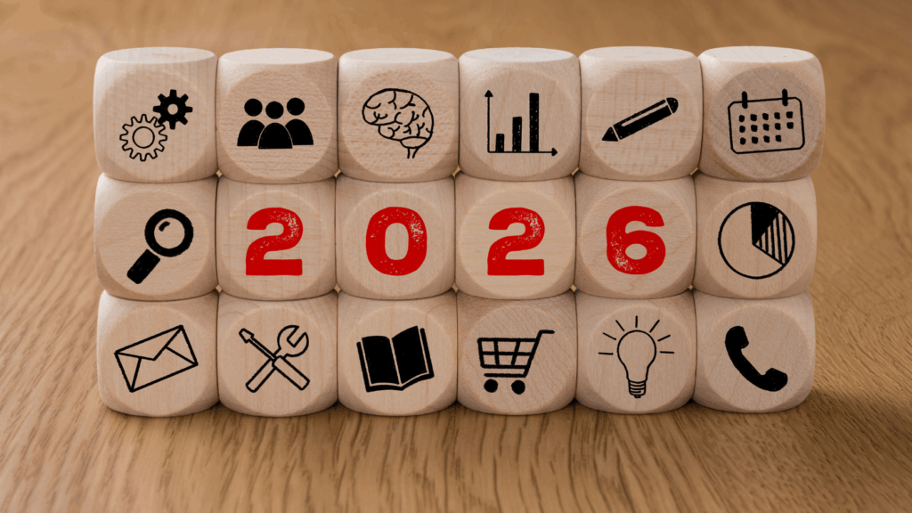 Wooden blocks arranged in rows displaying icons for analytics, people, AI, growth, planning, and communication, with the year “2026” highlighted in red, representing business and cybersecurity planning for the year ahead.