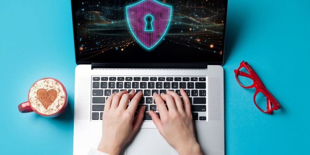 Hands typing on a laptop displaying a digital security shield, representing data protection and cybersecurity best practices.